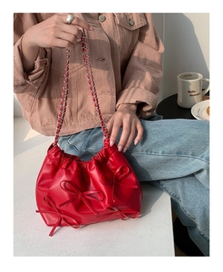 Close-up of red pleated shoulder bag with chain strap and three bow tie details