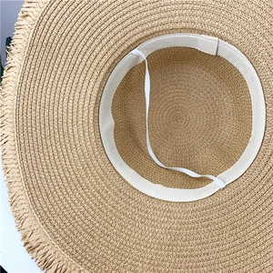 Detail of beige wide brim straw hat featuring raw fringe edges and adjustable chin strap