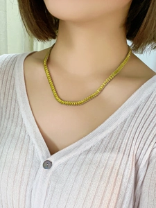 Close-up of golden square link necklace with colorful zircon on a white knit cardigan