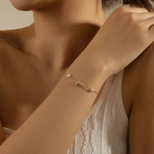 Close-up of a gold cross bracelet with shimmering crystals and white freshwater pearls