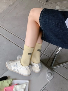 Close-up of yellow cotton crew socks with GOOD! embroidery on a model wearing sneakers