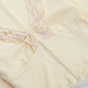 Detail of cream V-neck top showing ten transparent buttons and sheer mesh ruffle trim