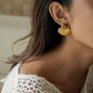 Close-up of a model wearing fan-shaped gold earrings with brown tiger eye stone inlay