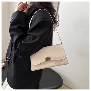 Detail view of a cream shoulder bag with gold metal buckle on a black blazer background