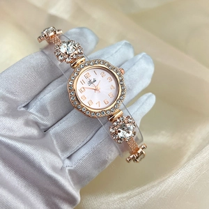 Close-up of rose gold watch with crystals on champagne silk held by gloved hand