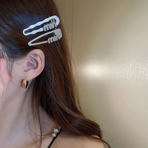 Close-up of silver rhinestone Miu letter hair clip worn by a model in warm light