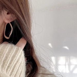 Close-up of a model wearing golden irregular geometric hoop earrings with metallic luster