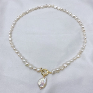 Detail shot of Baroque pearl necklace featuring a golden T-bar clasp on white silk fabric