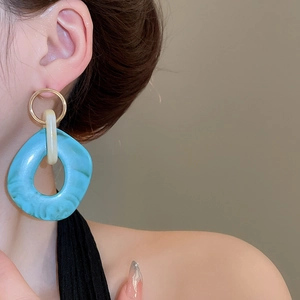 Detailed view of irregular turquoise and beige resin drop earrings on model's ear