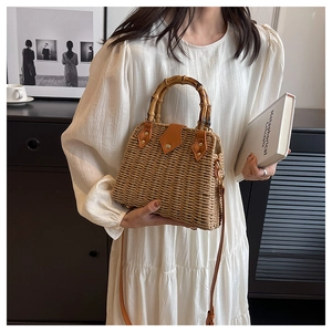 Detail of hand-woven straw bag featuring bamboo handles and premium brown leather trim