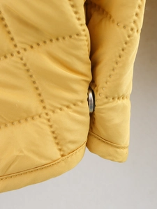 Détail de la veste matelassée jaune avec bouton métallique argenté et coutures précises