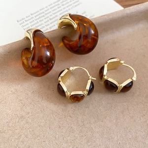 Close-up of amber resin C-shaped earrings and gold studs on a textured background
