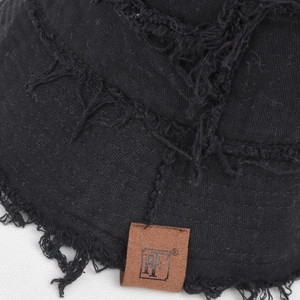 Detail shot of black frayed canvas hat with a leather patch logo and vintage distressed edge