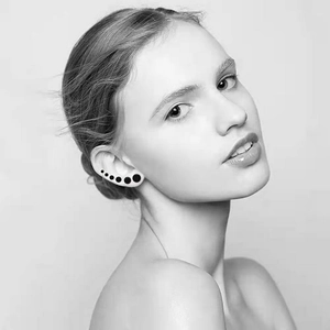 Set of five black round minimalist stud earrings arranged by size on a model's ear