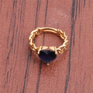 Macro shot of gold chain ring featuring a deep blue heart gemstone on wood surface