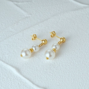 Close-up of dual pearl earrings with matte gold accents on textured stone