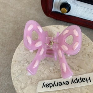 Pink acetate bow hair claw clip with woven thread detail on a marble display