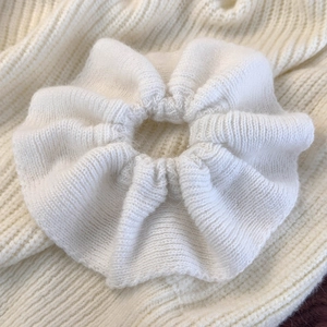 Macro detail of white knitted hair scrunchie showing soft textured fabric and wavy ruffles