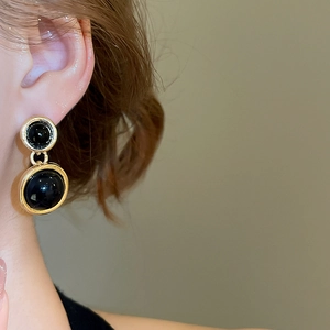Close-up of elegant gold and black resin circular drop earrings worn by a model