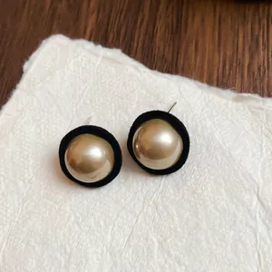 Retro round gold pearl earrings with black flocked edges on a textured paper background