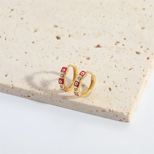 Gold evil eye hoop earrings with red beads and zircon on a beige stone surface