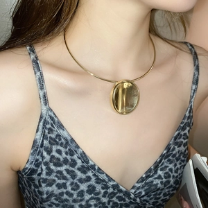 Close-up of golden necklace with a large oval mirror pendant worn by a female model