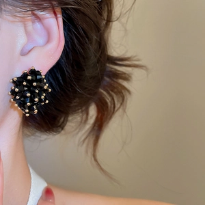 Close-up of irregular black crystal beaded earrings with gold accents on a model