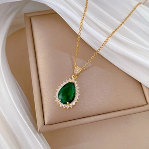 Macro view of golden necklace with green pear-shaped gemstone pendant on a jewelry box