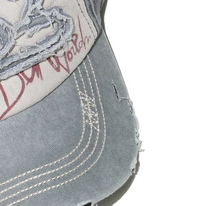 Macro shot of washed cotton baseball cap showing distressed brim and red script embroidery