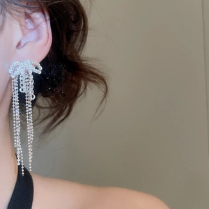 Close-up of a silver bow earring with sparkling rhinestones and long fringe tassel on ear