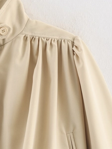 Detail of beige jacket collar showing delicate pleats and a single matching button