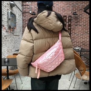 Pink quilted down waist bag with woven zipper pull worn cross-body on a beige puffer jacket