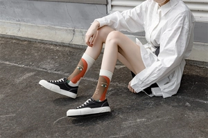 Detail shot of white crew socks featuring abstract artistic face patterns on a model