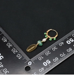 Detail view of pearl earring with green beads and handmade tag next to a scale ruler