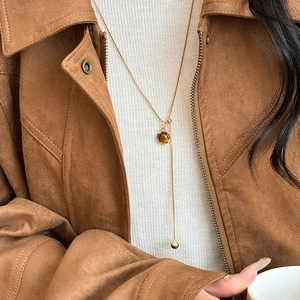 Vintage Y-shaped gold necklace with brown tiger eye stone pendant on brown suede jacket