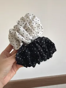 Detail of pleated polka dot scrunchies in black and white chiffon fabric held by hand