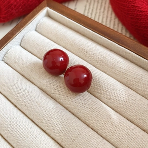Close-up of bright red glossy ball studs displayed in a cream velvet jewelry box
