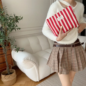 Detail of red and white striped cosmetic bag with text label held by a model