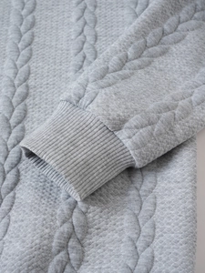 Detailed close-up of light grey knit sweater showing textured diamond pattern and ribbed cuffs