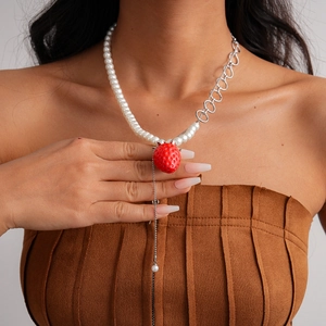 Detail of strawberry pendant necklace with asymmetrical pearls and silver chain worn by model