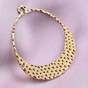 Close-up of golden crescent pendant with hammered texture on pink silk background