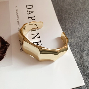 Detailed close-up of a wide gold open cuff bracelet with wavy geometric texture design