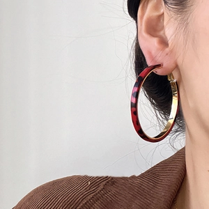Detail of model wearing large leopard print resin hoop earrings with gold metal accents