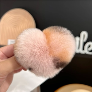 Detail of soft heart-shaped faux fur hair clip in pink and brown being held by hand