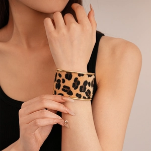Detail of wide leopard print bangle with gold trim worn on wrist by a model