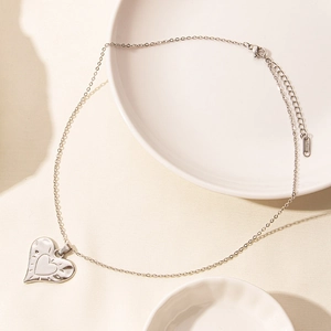 Macro detail of silver heart pendant with sunburst texture and lobster clasp on steel chain