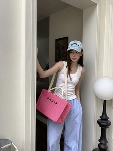 Close-up of pink straw tote bag with Paris embroidery and blue Los Angeles baseball cap
