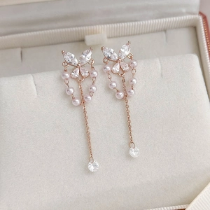 Close-up of rose gold butterfly earrings with zircon stones and pink pearl tassels