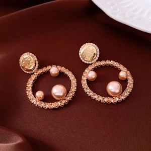Macro detail of 18K gold plated pearl earrings with embossed logo and silk background