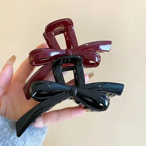 Elegant glossy bow hair claw clips in burgundy and black shown in a hand-held display